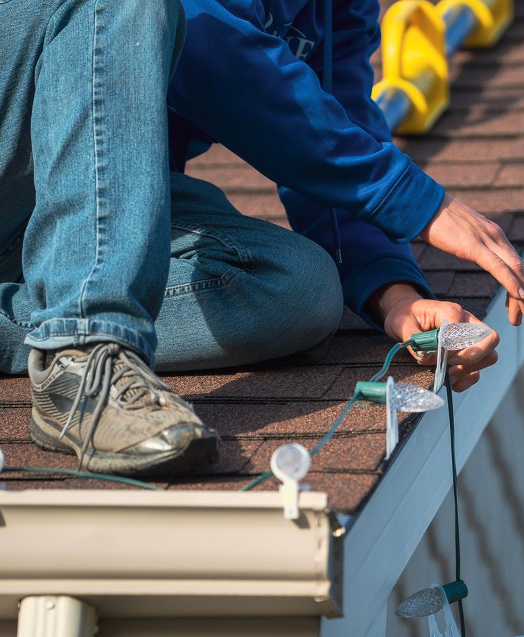 workmen on a roof installing holiday lighting on a house